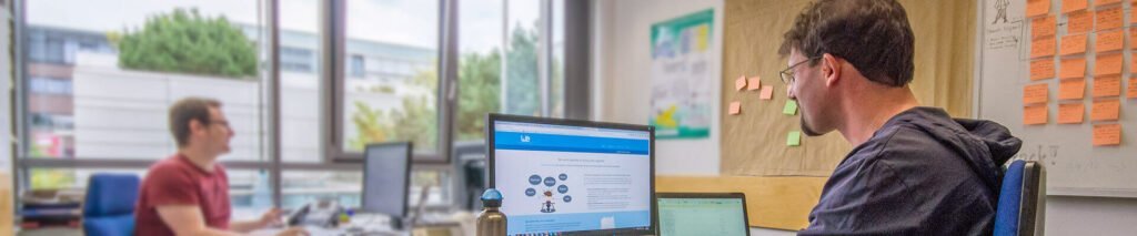 Thorsten Reitz and Simon Templer, founders of wetransform, sit at the desks in wetransform's offices at the Fraunhofer Institute in Darmstadt on a sunny day in 2014. Visible on Thorsten's monitor is an early version of wetransform's website.