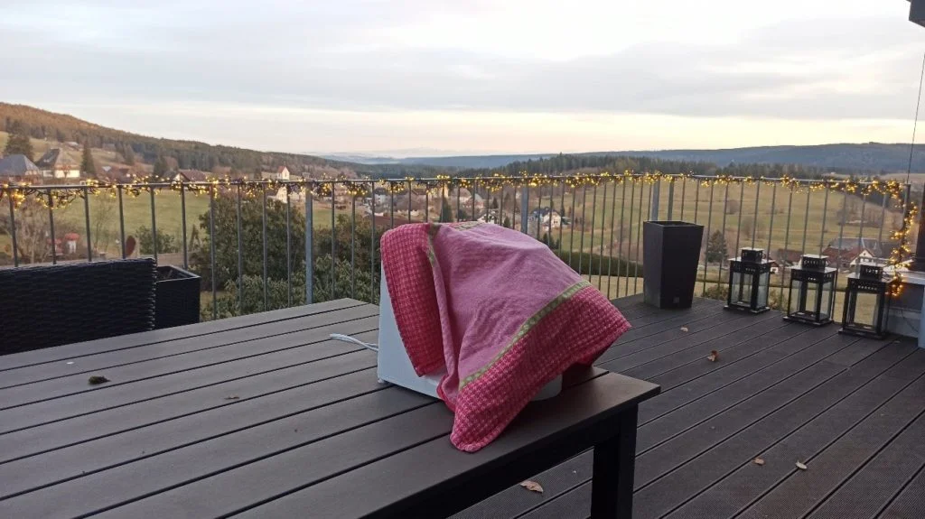 A stand mixer, partially covered by a pink-and-green cloth, stands on an outdoor patio table.