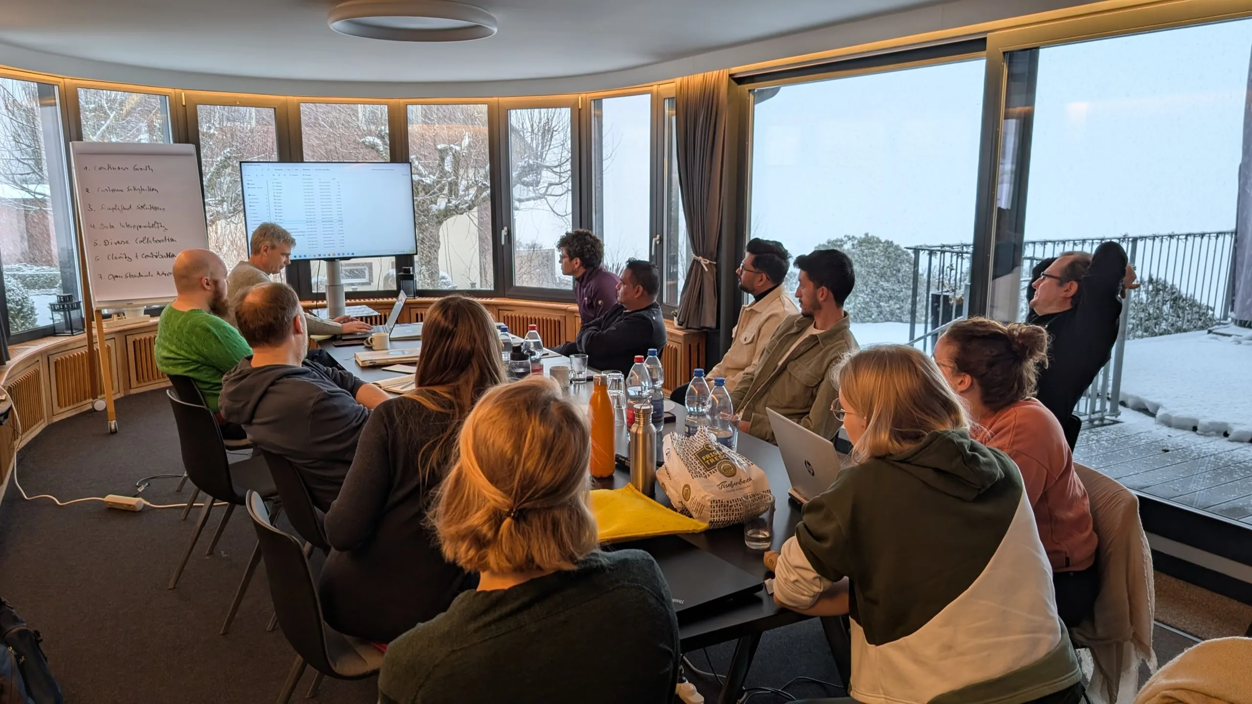 The wetransform team sits at a conference table during the 2025 offsite. Through the room's many windows the snow outside is clearly visible.