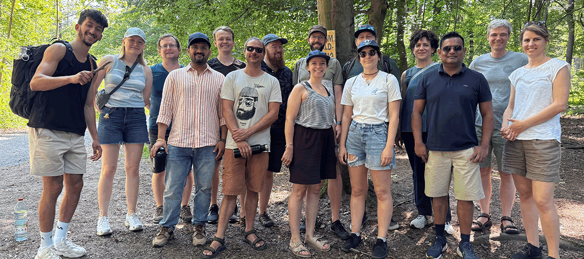 Group photo from the 2025 wetransform Summer Offsite. 15 members of the wetransform team stand in a forest, organised in two rows, smiling at the camera.