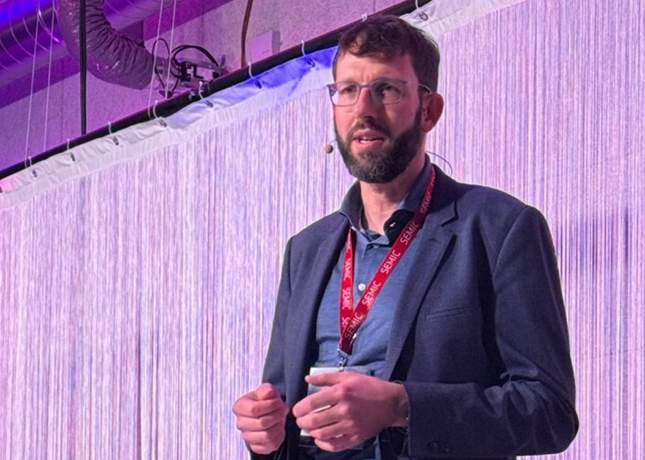 Thorsten Reitz, a bearded man with dark hair and glasses, is presenting at SEMIC 2025. He is wearing a blue button-down shirt and jacket, as well as a red SEMIC lanyard, and is wearing a professional head-worn lavalier microphone.
