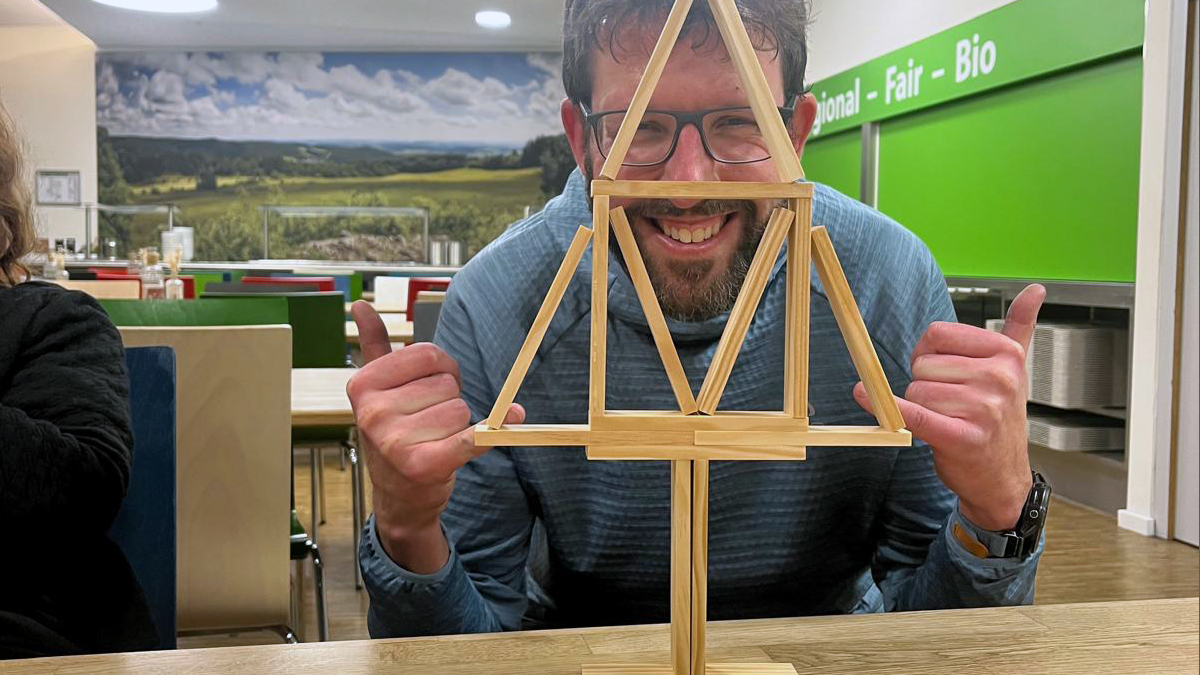 wetransform CEO Thorsten Reitz grins broadly at the camera from behind an impressively balanced construction of wooden blocks he has built into the shape of an evergreen tree. He is making triumphant gestures with both hands.