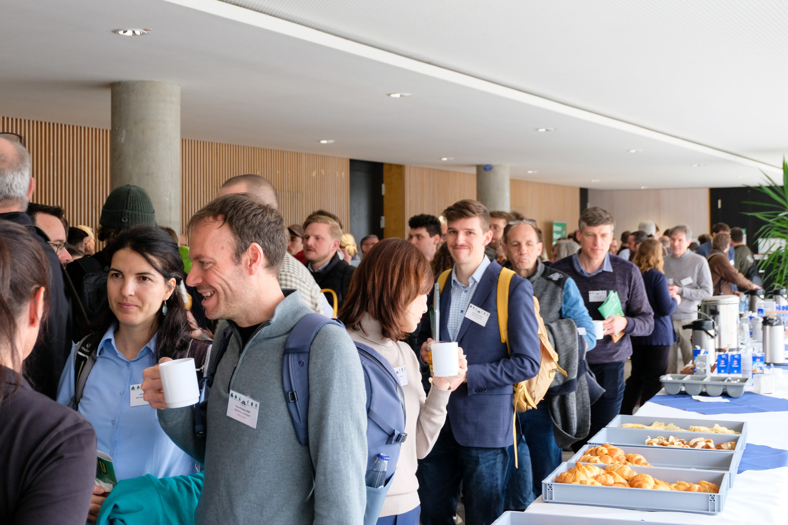SmartForest 2026 attendees fill the foyer during a break, chatting beside a long table laden with drinks and pastries